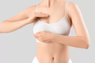 A woman in a white bra top gently touches her breast, reflecting on her breast implant or reduction journey.