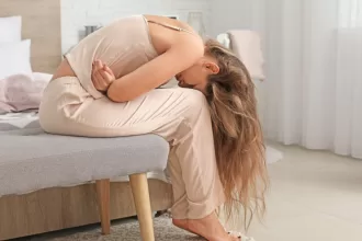 A woman sitting on a bed, her head in her hands, reflecting the emotional impact of endometriosis surgery.