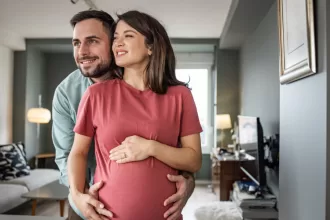 A pregnant woman and man stand together in a cozy living room, symbolizing hope and family after fertility surgery.