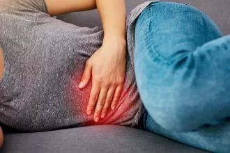 A woman sitting on a couch, visibly in discomfort, reflecting on her recovery after fibroid removal surgery.