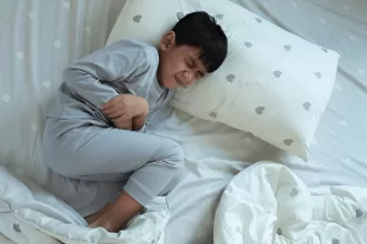 A young boy resting on a bed surrounded by pillows, recovering after Hirschsprung Disease surgery.