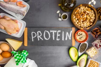 Collagen protein powder in a scoop, surrounded by healthy food sources like fish, eggs, and leafy greens, on a wooden table.