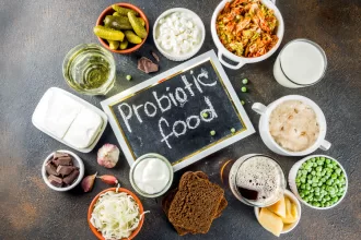 Colorful arrangement of prebiotic-rich foods including bananas, garlic, onions, asparagus, oats, and legumes on a wooden table.