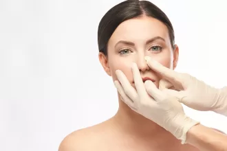 A woman undergoing rhinoplasty surgery as a doctor carefully performs the nose reshaping procedure.