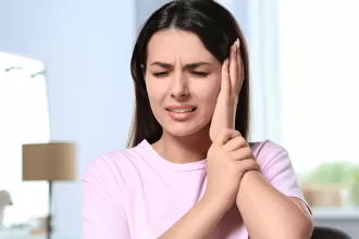 A woman holds her ear in discomfort, highlighting the impact of ear pain related to stapedectomy surgery.