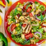 Rainbow plates of vegan-keto food, featuring avocado, nuts, seeds, leafy vegetables and coconut oil laid out neatly on a rough wooden table.
