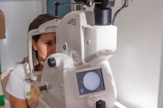 A woman examines an eye exam machine, highlighting the importance of vision care post-vitrectomy surgery.