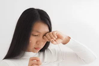 A woman with a concerned expression holds her head while looking at her phone, reflecting on her diabetic retinopathy surgery.